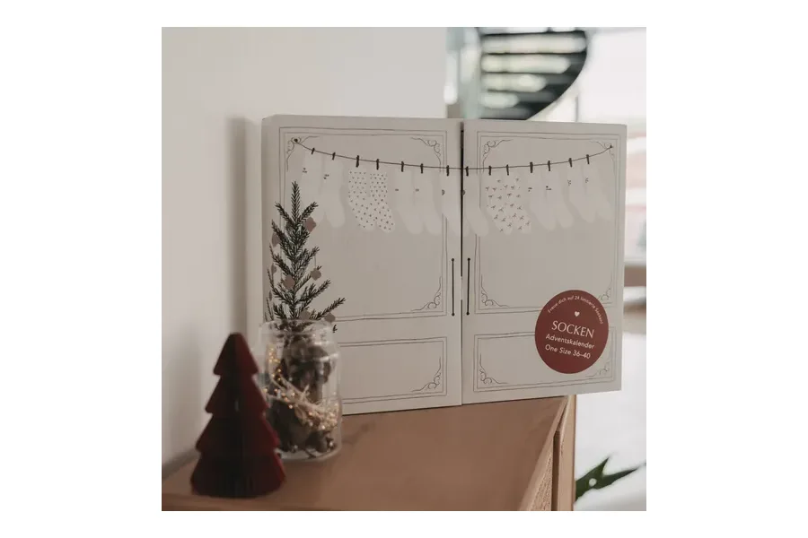 Cremefarbener von Herzen Socken-Adventskalender 2026 mit gezeichneter Sockenleine auf einer Kommode